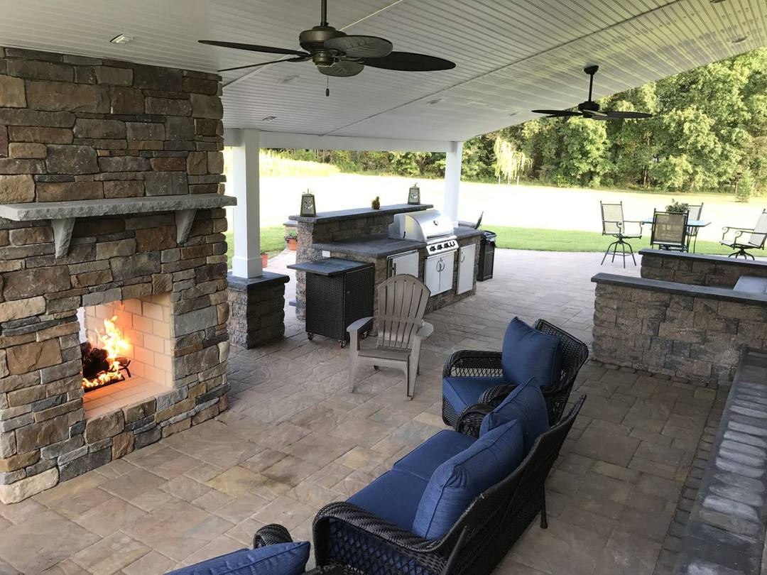 Stone outdoor fireplace beside an outdoor kitchen on a covered patio