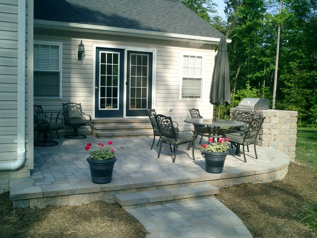 Raised paver patio with a built-in grill island behind a home