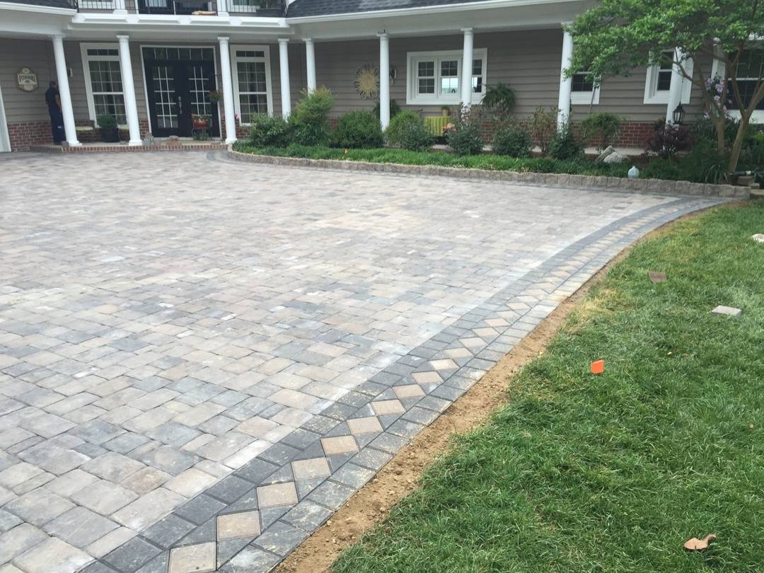 Paver driveway with a charcoal border inlay curving past the lawn