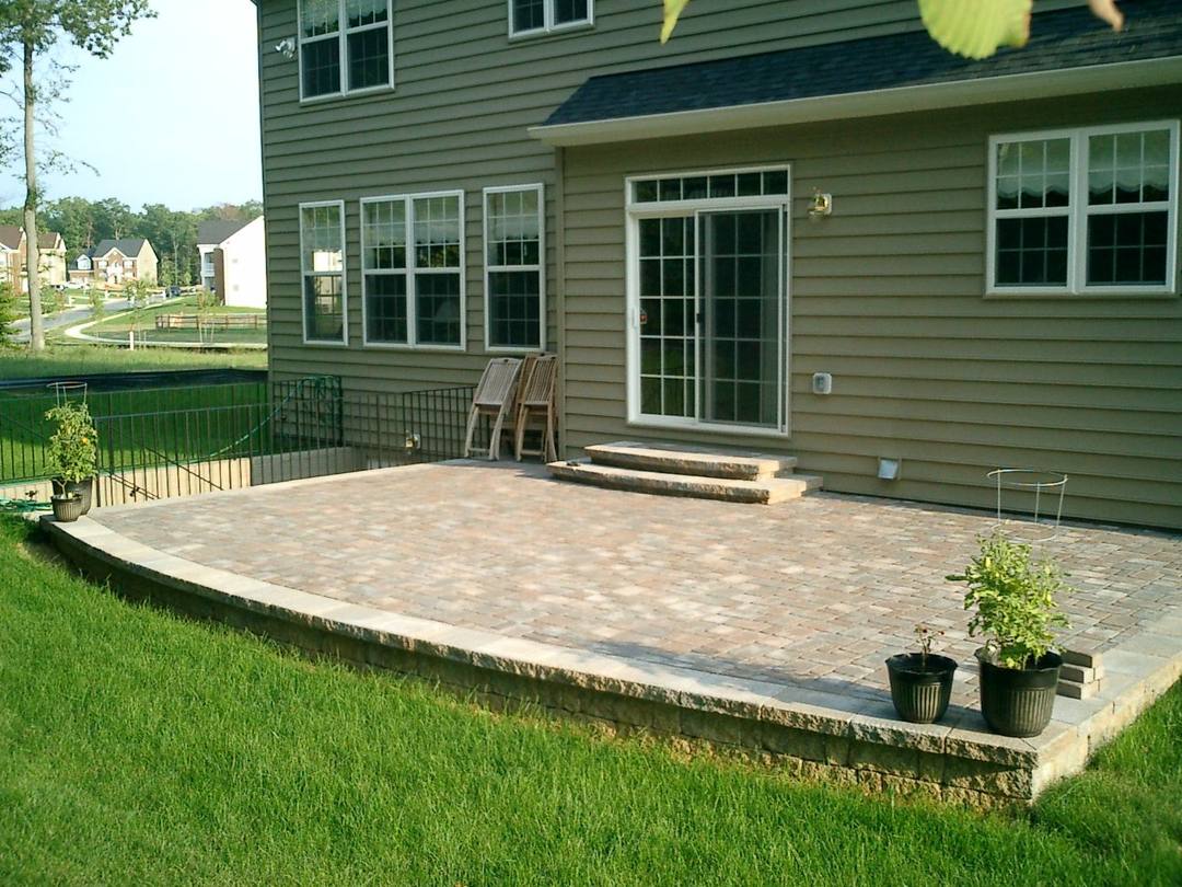 Raised paver patio with a low seat wall behind a two-story home