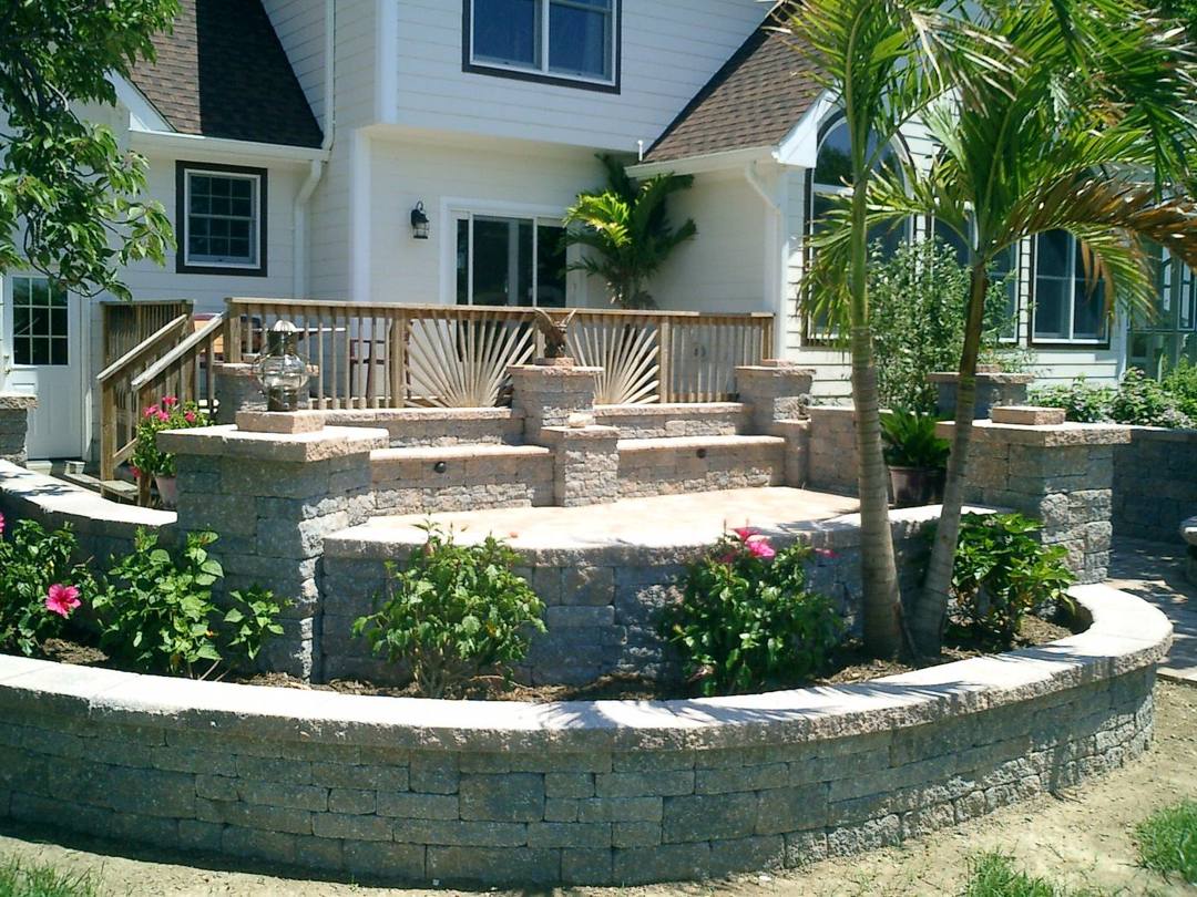 Paver patio with palms and a curved seat wall in front of a home