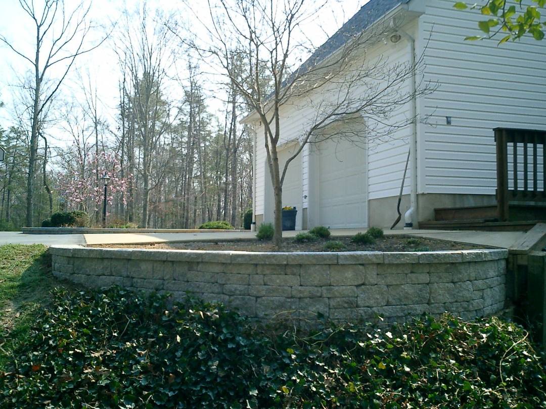 Curved block retaining wall around a planting bed beside a garage