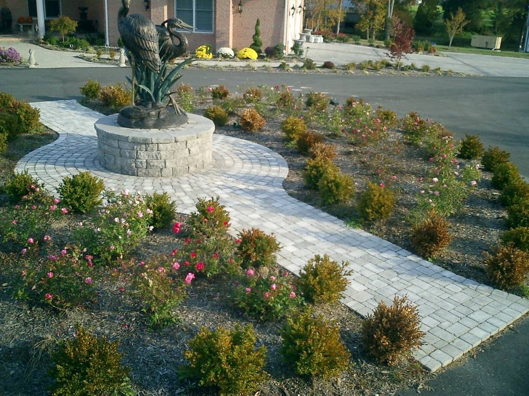 Paver walkway circling a fountain sculpture through a garden bed