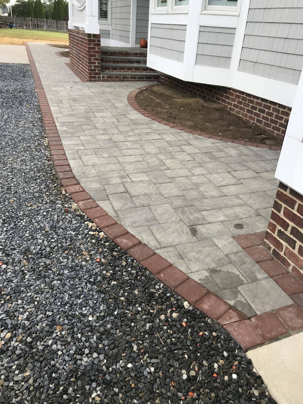 Paver walkway with a red brick border beside gravel