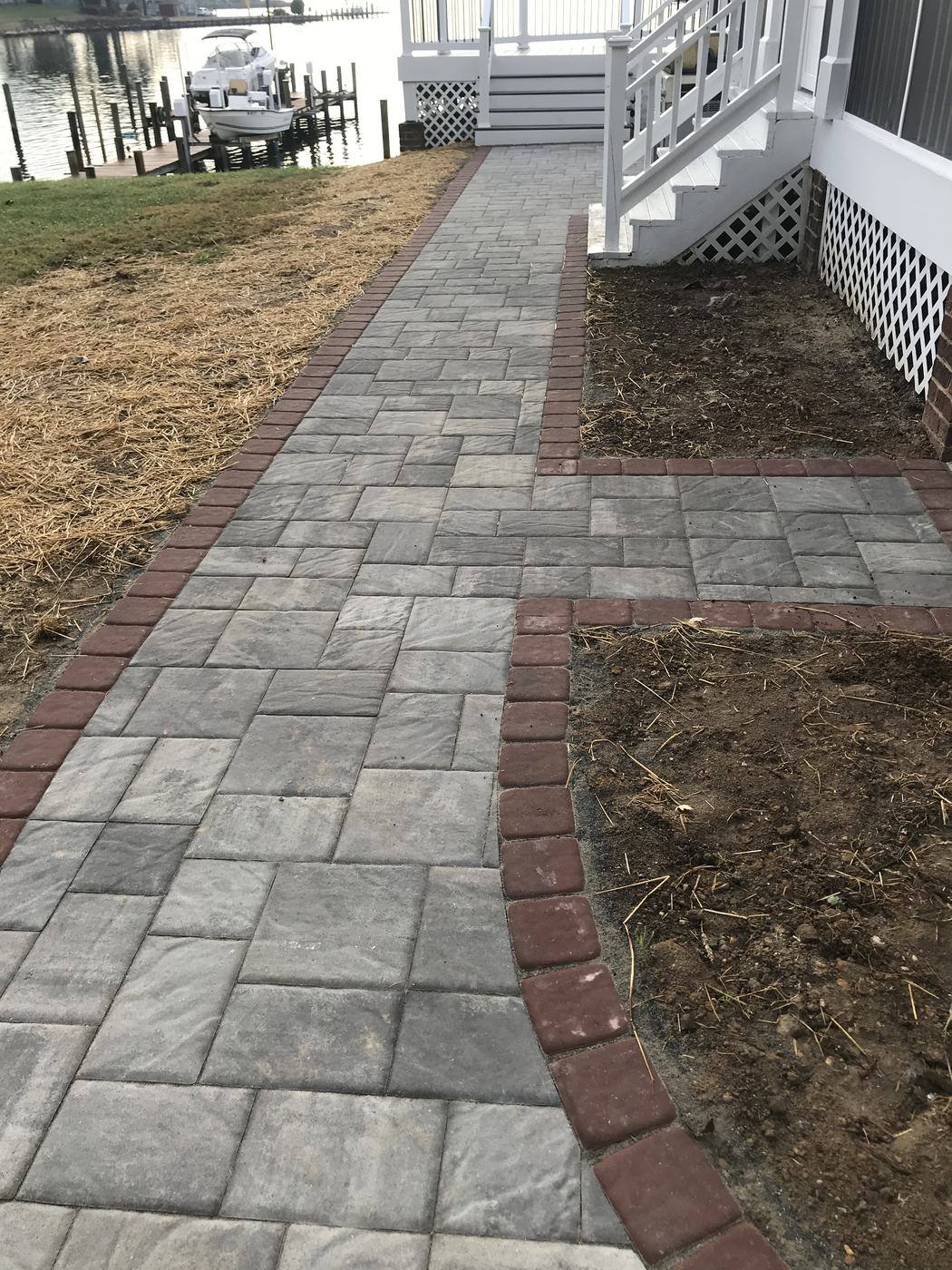 Gray paver walkway with a red border leading toward the waterfront
